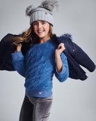 A smiling girl wearing a Dusty Blue Willow Top with a stylish hat and jacket, showcasing cozy children's fashion.