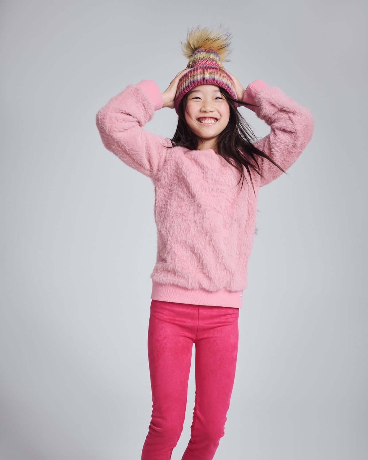 Girl wearing the Ivy Rose Willow Top with a playful expression, styled with pink leggings and a colorful hat.