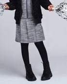 Girl wearing a Black Boucle Yoke Pleated Skirt with a black jacket and boots, perfect for active outdoor play.