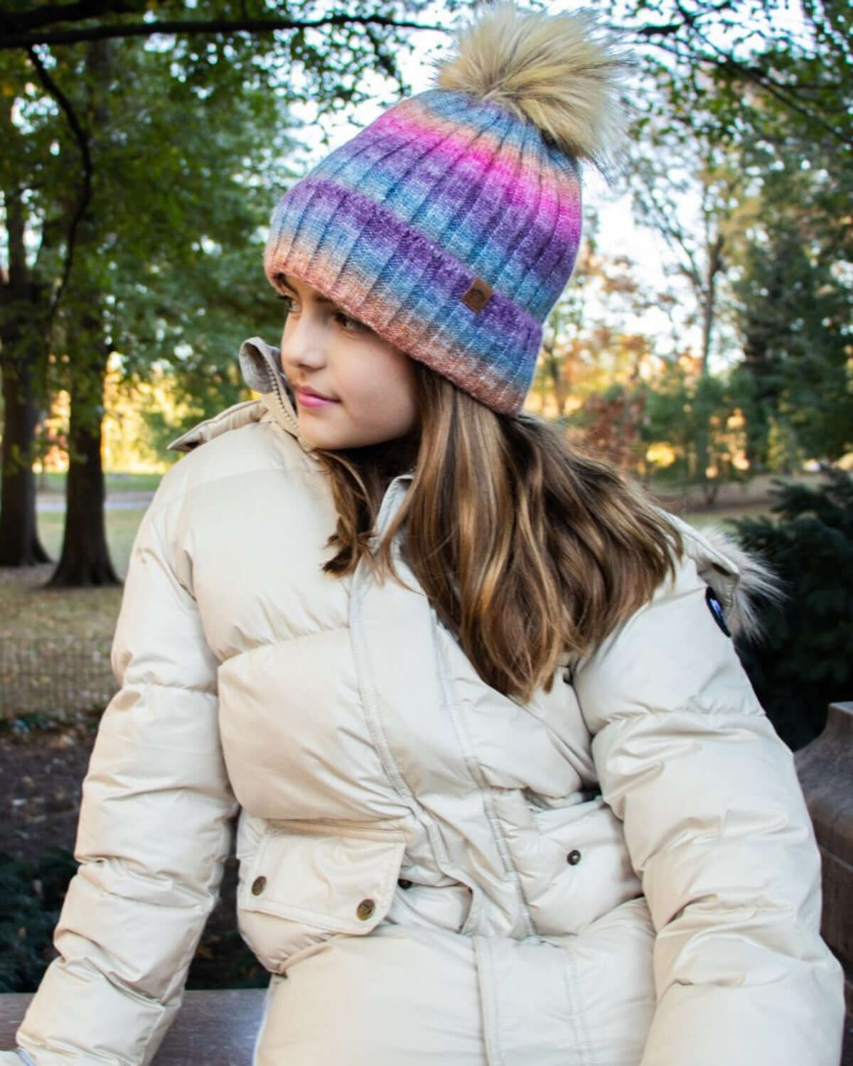 Girl wearing an Ivory Expedition Puffer Coat with a colorful knitted hat in a park setting.