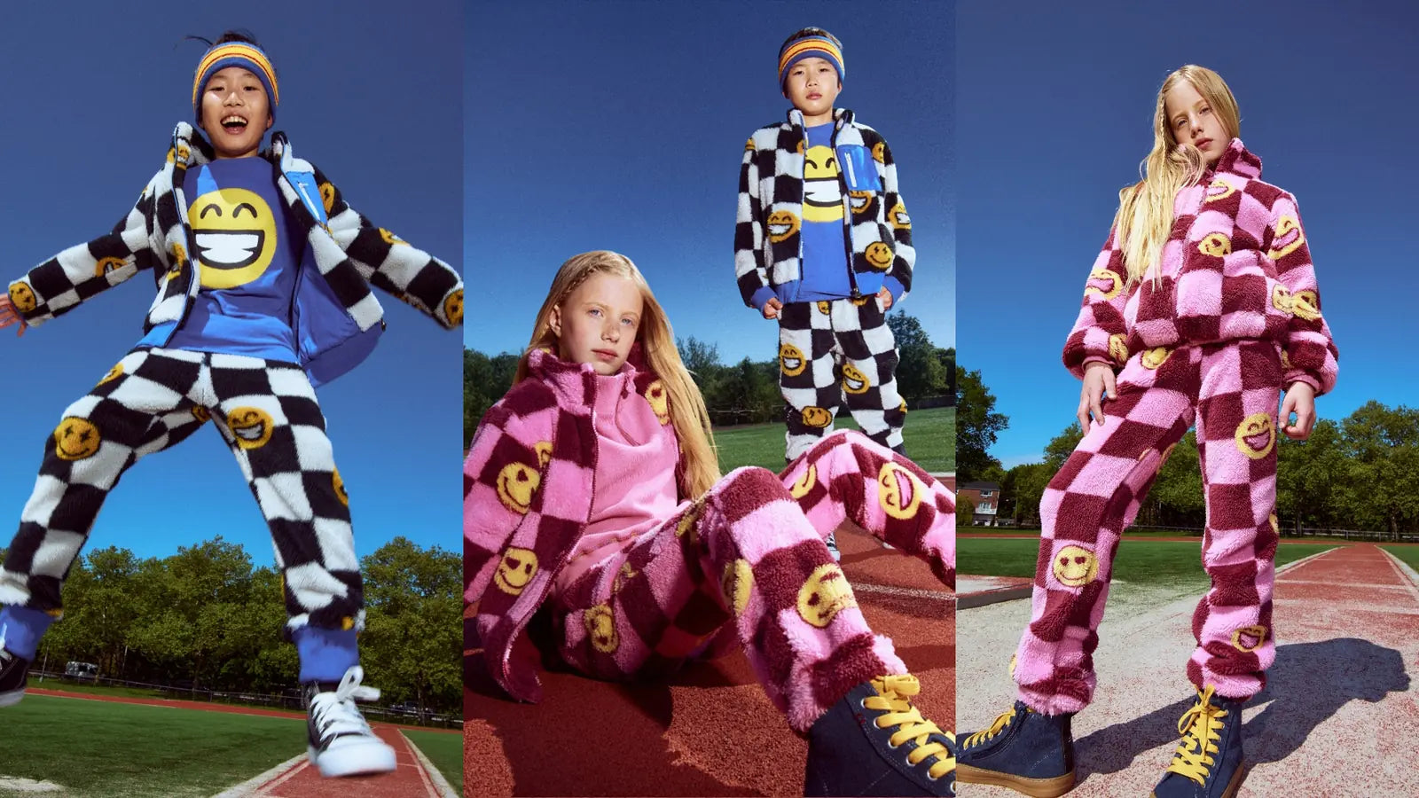 Three outdoor photos of children modeling matching checkered emoji tracksuits. The left child wears a black-and-white checkered outfit with yellow smiley faces and a blue hoodie.