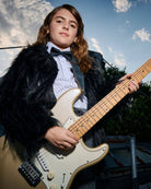 Child wearing a black silk bow tie while playing an electric guitar outdoors.