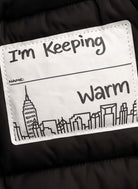 Kids Black Puffy Coat label showing "I'm Keeping Warm" with city skyline design.