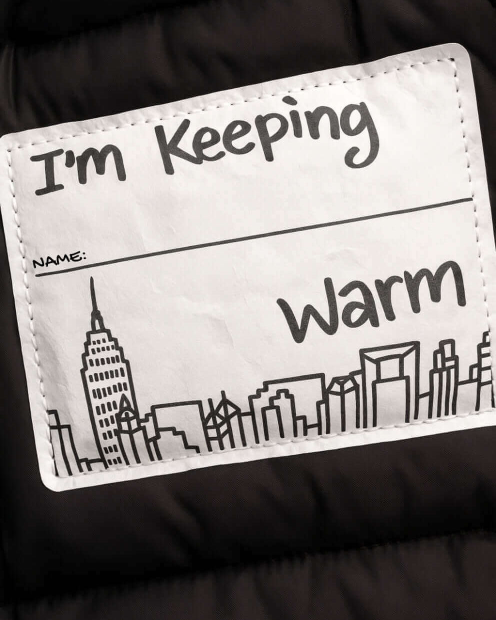 Black Slim Puffy Coat label that says I'm Keeping Warm with a city skyline illustration.