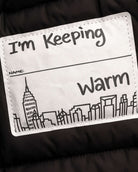 Close-up of the label on the Glitter Black Slim Puffy Coat stating "I'm Keeping Warm" with a city skyline design.