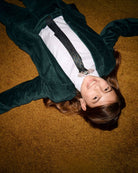 A stylish kid in an evergreen blazer, playfully lying on a rich textured floor, showcasing modern kids clothing flair.