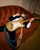 Chic kid rocking a gold guitar on a plush couch, stylish in a midnight velvet blazer—ready to steal the show!