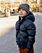 Stylish kid in a camo puffer jacket and grey beanie, ready for winter escapades in high-quality kids clothes!