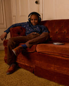Chill kid in stylish brown commuter twill pants and a cool shirt, rocking headphones on a vintage couch, ready for fun!