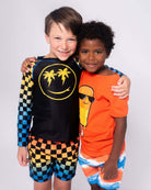 Two kids showing off their vibrant summer styles—one in a palm-print tee and the other in an orange popsicle shirt.