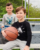 Two stylish boys on bleachers, one proudly holding a basketball, showcasing kids' clothes in action.