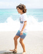 A happy boy splashes in ocean waves wearing the Madagas-Star Graphic Tee and stylish swim shorts, perfect for summer fun!