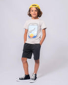 Playful boy in a window seat graphic tee and shorts, ready for adventures in kids clothes.