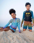 Kids rocking vibrant checkerboard swim styles on the beach, showcasing fun summer vibes and high-quality swimwear.