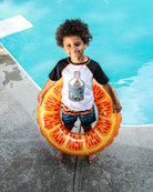 Young boy in a ship-in-a-bottle rash guard, holding a fruity pool float by the refreshing water.