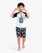 A stylish boy in a ship-in-a-bottle rash guard and playful pirate shorts, ready for a fun day at the beach!