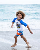 A joyful boy runs along the beach in colorful swim trunks and a playful tee, ready for sunny adventures!