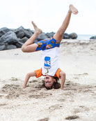 Joyful kid in a fun soda Rash Guard doing a handstand on the beach, paired with vibrant swim trunks!