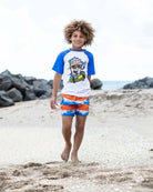 Cool kid in a blue Soft Served Rash Guard and fun swim trunks, ready for beach adventures under the sun!
