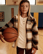 Stylish boy in a cozy plaid jacket and thermal henley holding a basketball, ready for fun in high-quality kids clothes.