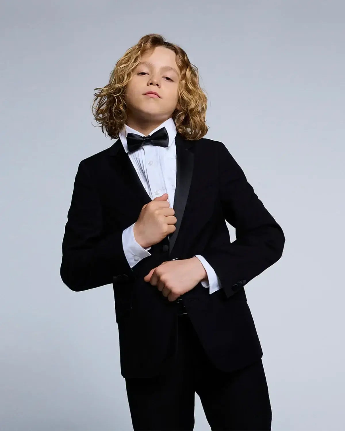 Stylish kid in a black tuxedo with a bow tie, showcasing high-quality kids clothing for formal occasions.