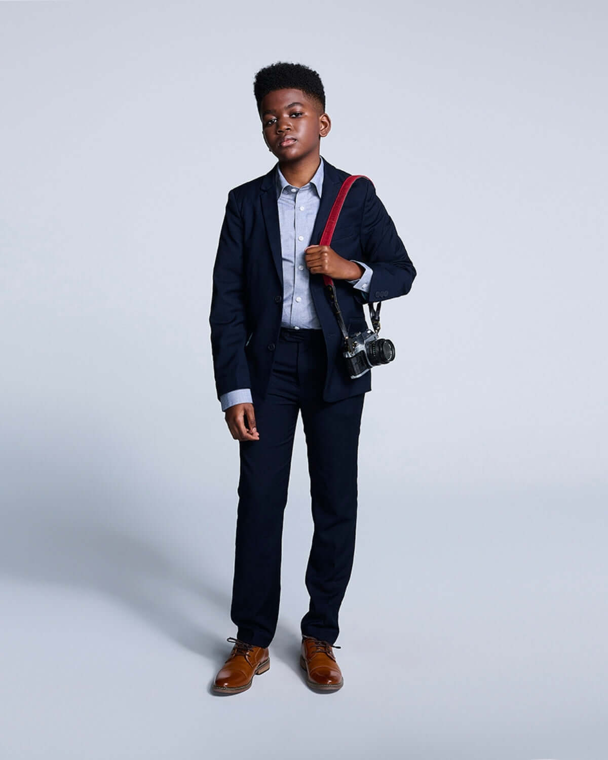 Boy wearing a grey standard button down shirt with a suit and holding a camera, perfect for stylish occasions.
