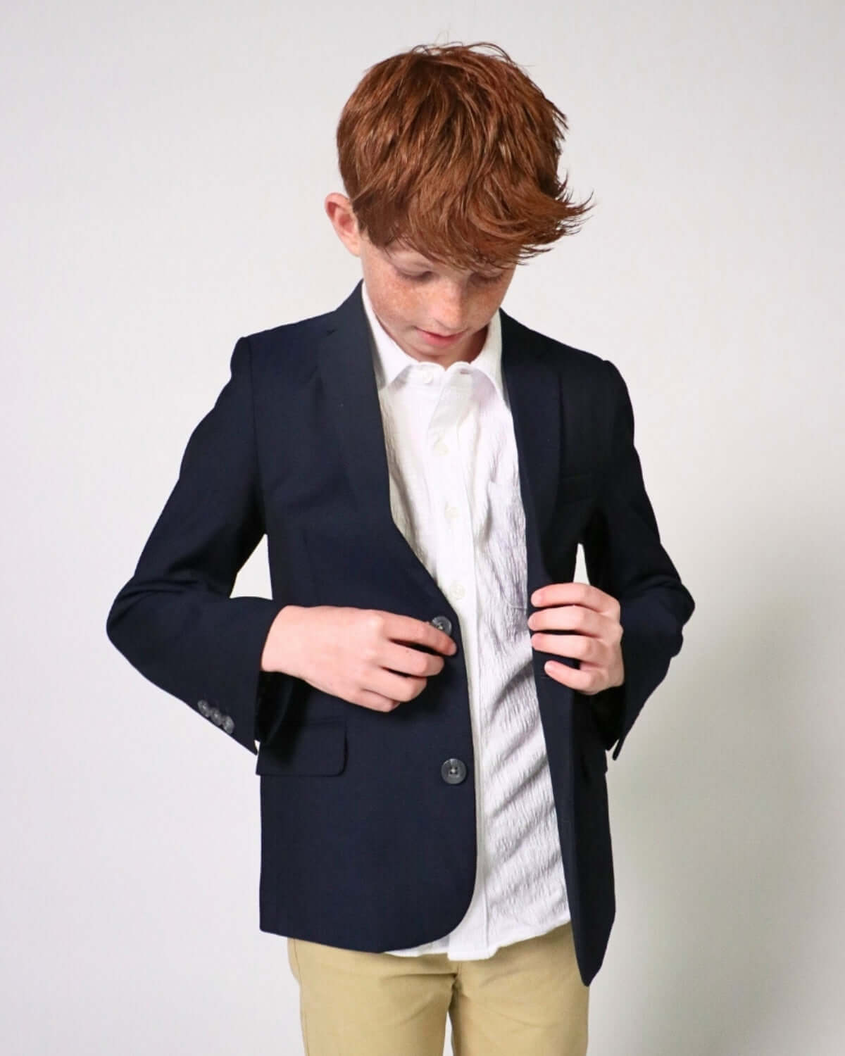 Boy adjusting buttons on an Indigo Suit Blazer over a white shirt, showcasing fine tailoring and polished style.
