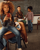 Three stylish kids in playful outfits, showcasing Lakeside Plaid and leopard print in a fun classroom setting.