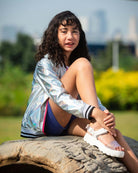 Chic girl in shiny bomber jacket and sandals, rocking playful summer vibes in a sunny park. Perfect kids' clothes for style and comfort!