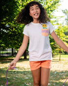 Joyful girl in peach shorts and playful tee, ready for summer adventures and back-to-school fun in durable kids clothes.