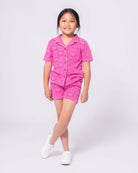 Stylish girl in pink heart-patterned shorts and matching shirt, ready for beach fun in high-quality kids clothes!