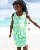 Girl in a sunny blue dress with yellow daisies, enjoying beach fun in stylish kids clothes for summer adventures.