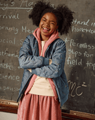 Smiling girl in Blue Prism Queens Bomber, pink hood, cozy quilted style; perfect for school or play time adventures.