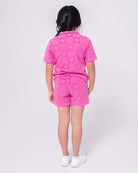 Bright back view of a girl in a playful pink resort shirt and shorts, showcasing stylish heart patterns for kids' summer fun!