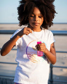 A girl with curly hair blows bubbles while wearing a playful White Circle Tee, capturing summer magic and joy.
