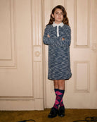 Stylish girl in navy tweed polo dress, showcasing playful confidence with chic accessories and a fun backdrop.