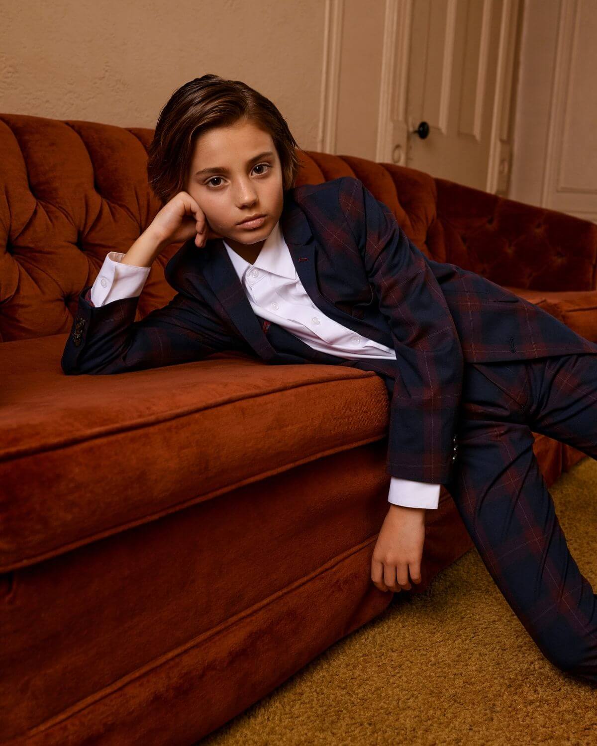 Kid stylishly posing in a Navy/Cranberry Plaid Stretchy Mod Suit on a cozy couch.