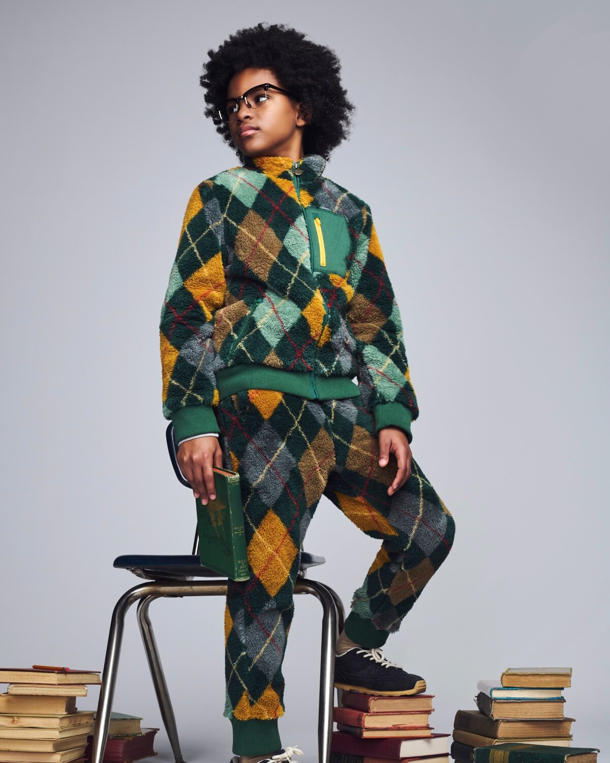 Person wearing a colorful argyle pattern outfit sitting on a stack of books.
