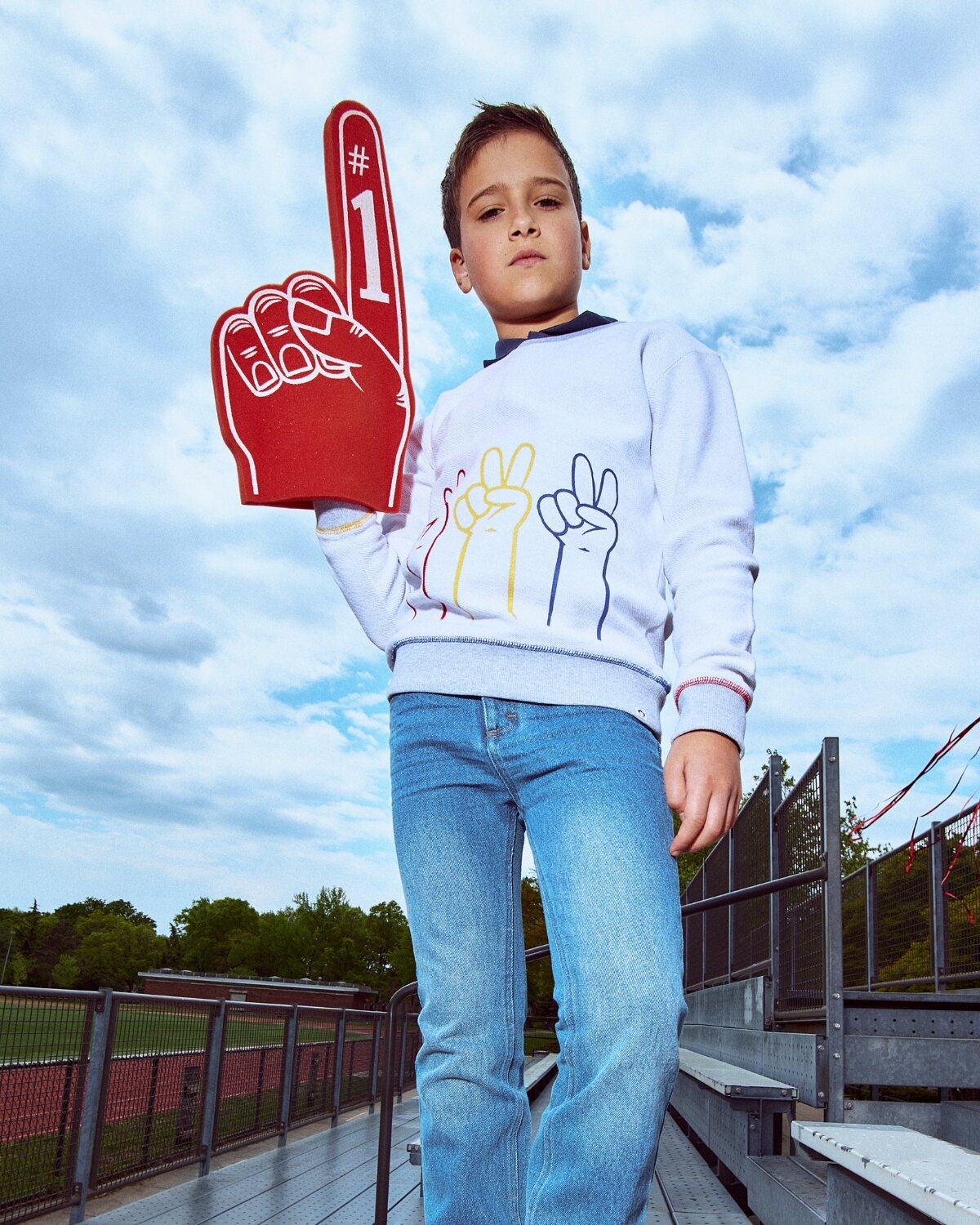 Child holding a foam finger with '#1' against a cloudy sky