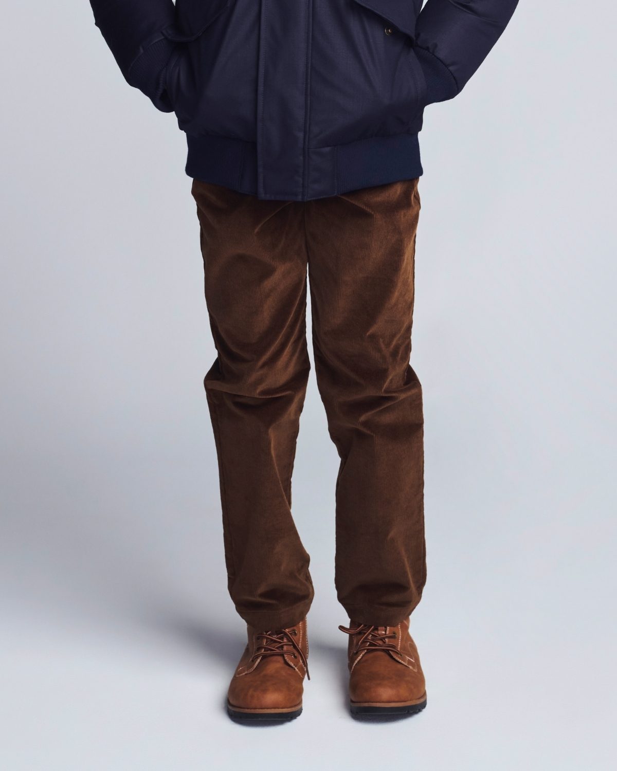 Person wearing a navy jacket, brown pants, and brown boots on a light gray background