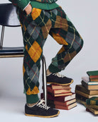 Person wearing argyle patterned pants and black shoes standing on a stack of books.