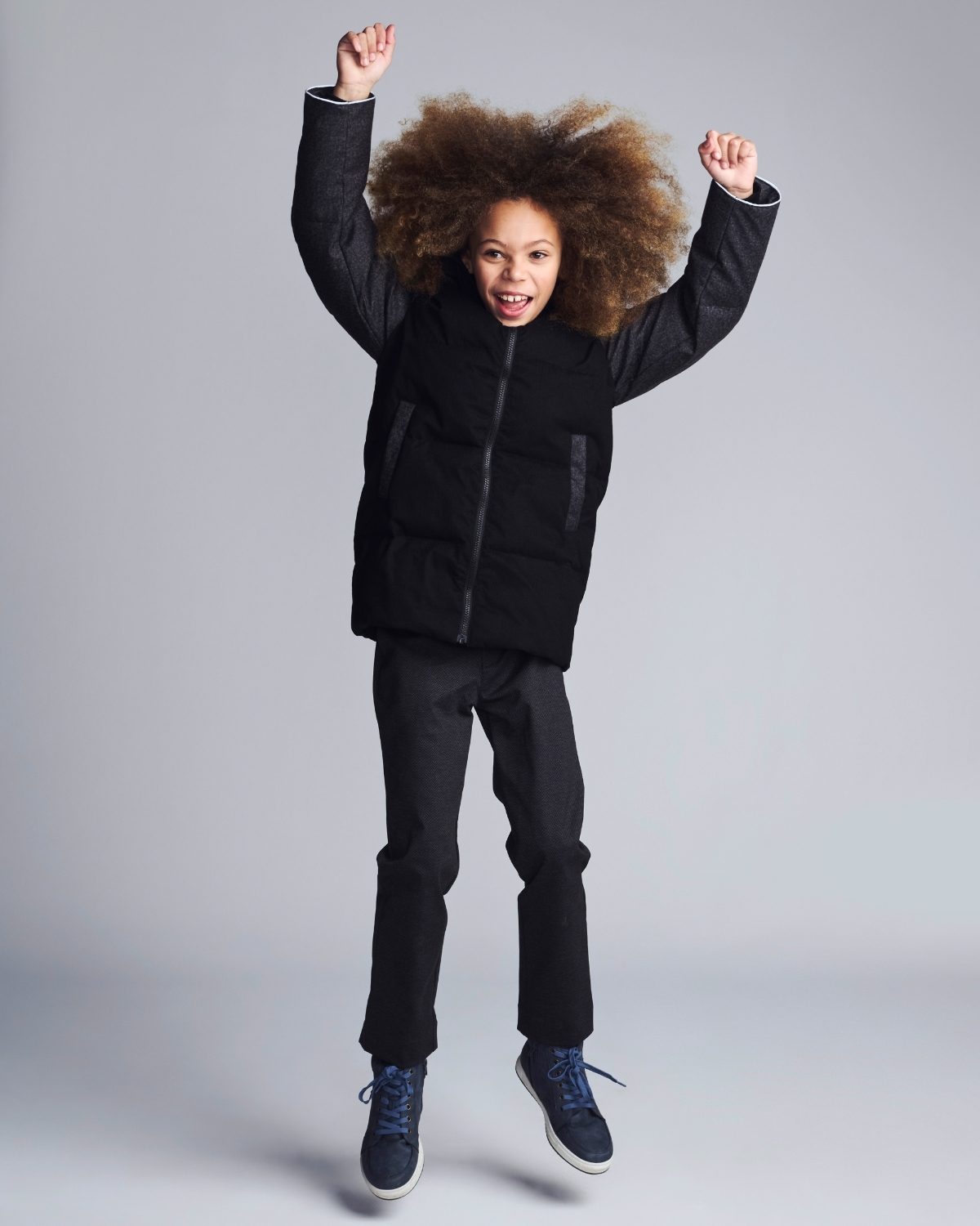 Child wearing a black jacket and pants on a gray background