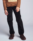 Person wearing black pants and brown shoes on a light gray background