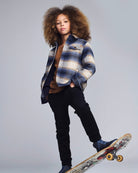 Person wearing a plaid jacket and black pants, standing on a skateboard against a gray background