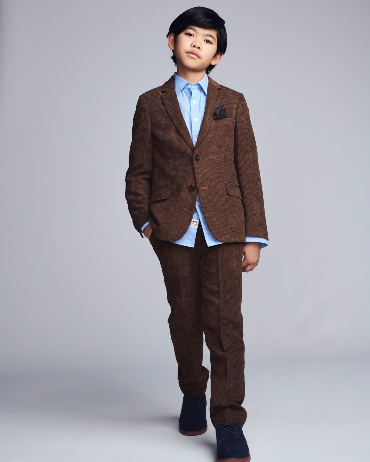 Young boy wearing a brown suit with a blue shirt on a gray background
