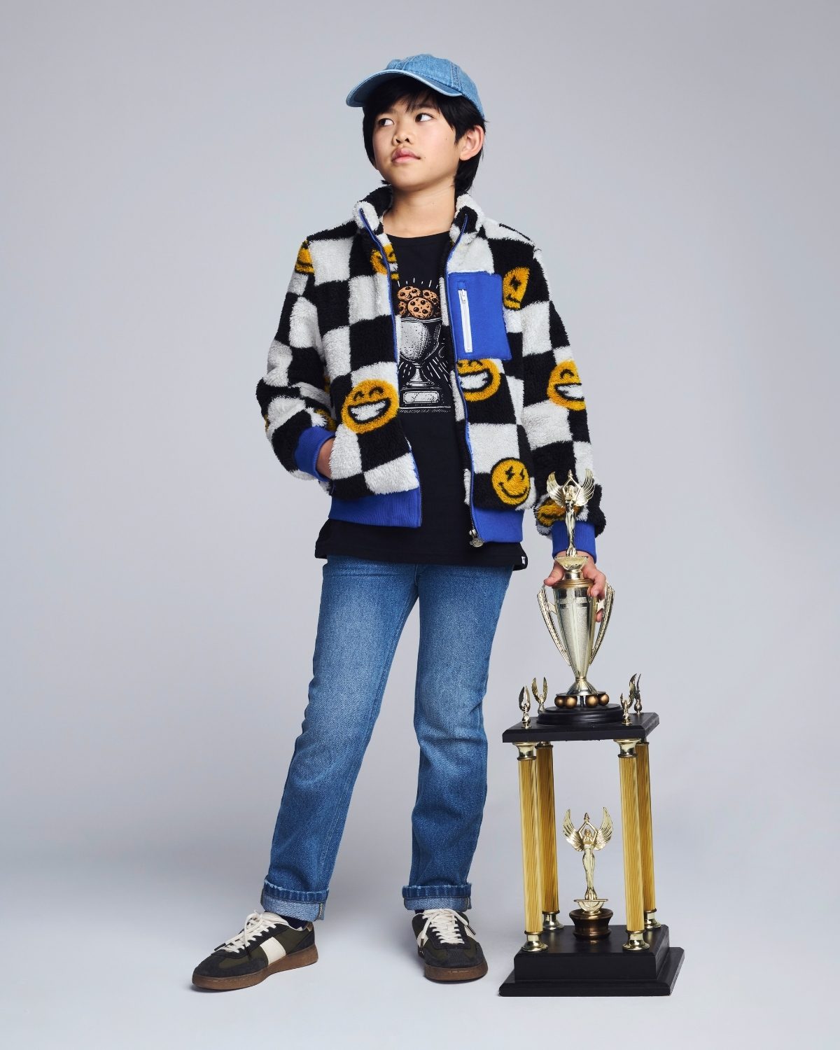 Person wearing a checkered jacket with smiley face patterns, holding a trophy on a gray background