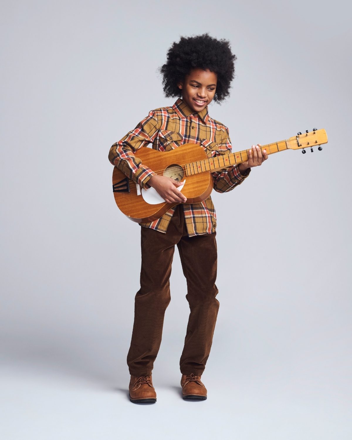 Person playing a wooden guitar against a plain background