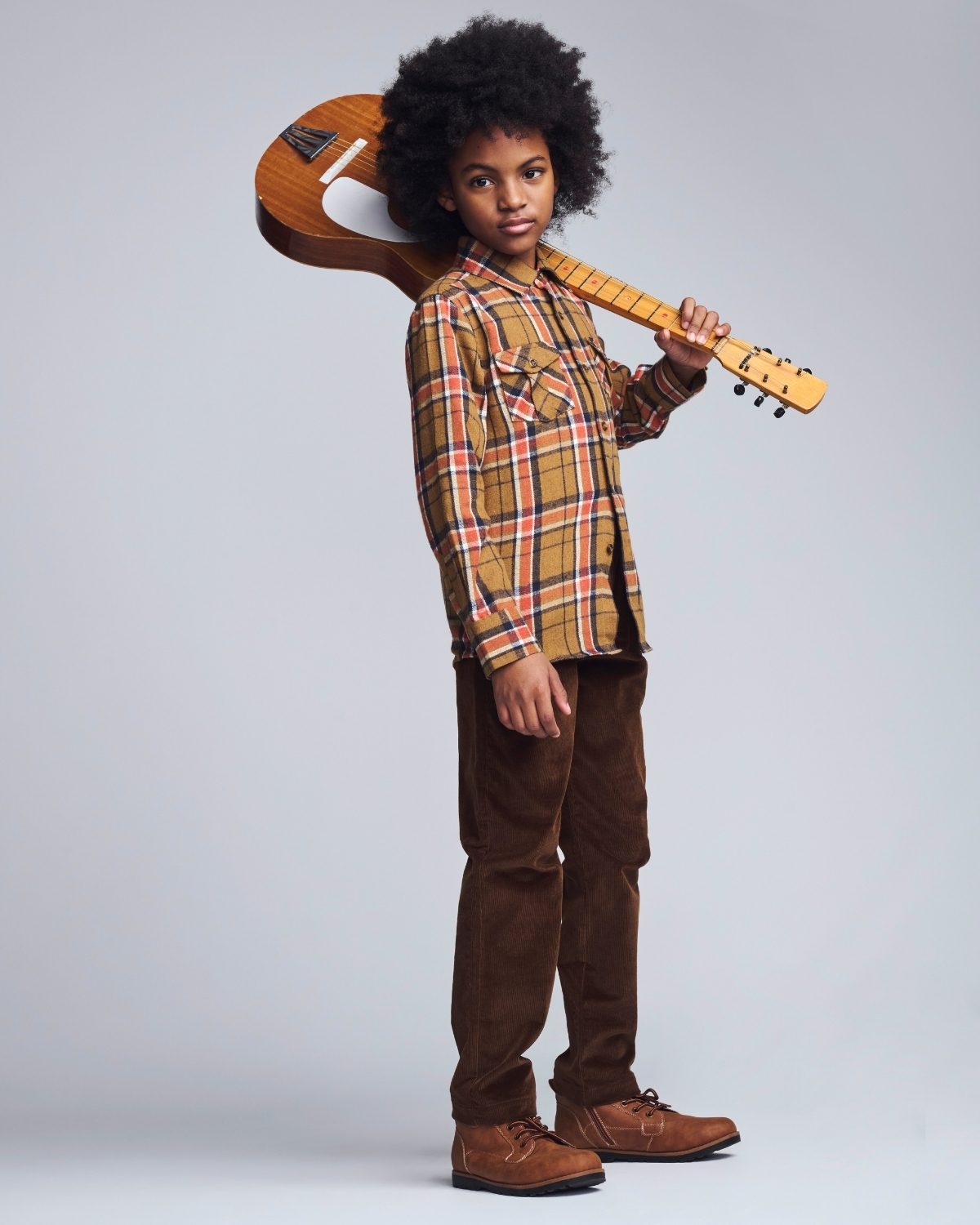 Child holding a guitar against a plain background
