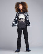 Person wearing a checkered shirt over a graphic t-shirt with black pants on a gray background