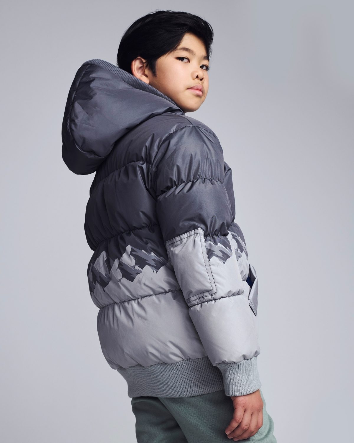 Child wearing a gray puffer jacket on a plain background